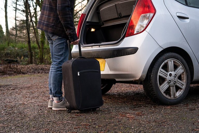 A person loading luggage into an open car trunk