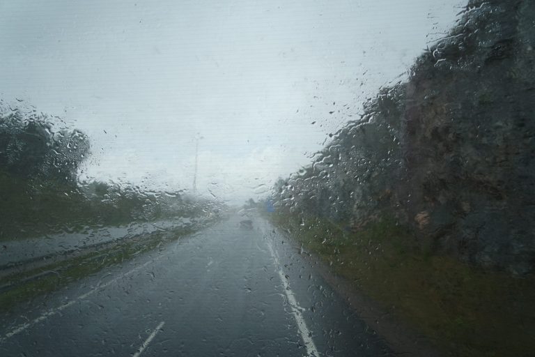 Road and trees seen through a rain-covered vehicle windshield